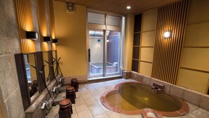 A spa area with a large hot tub, a row of sinks, and a sliding glass door leading to an outdoor area. - Konaya Hotel (Kofu)
