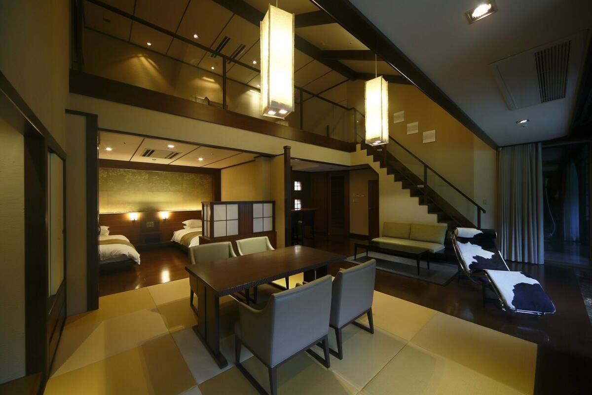 A hotel room with a dining area, a sofa, a lounge chair, and a staircase.