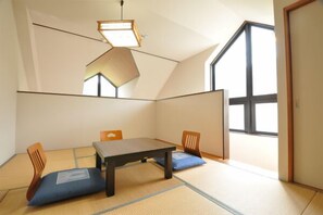 Ein Zimmer mit Tatami-Boden, einem niedrigen Tisch und zwei Stühlen.