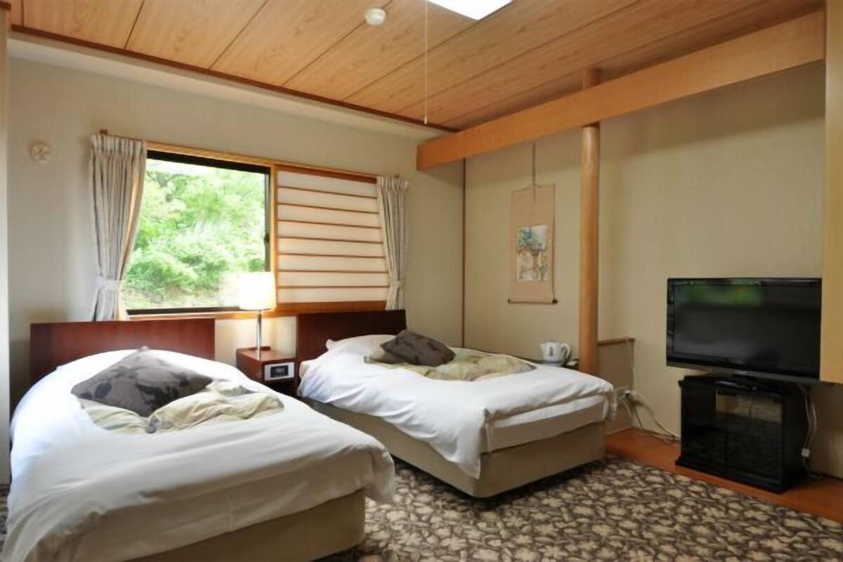 Ein Hotelzimmer mit zwei Betten, einem Fernseher, einem Fenster mit Vorhängen und einem Bild an der Wand.
