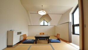 A room with tatami flooring, a low table with cushions, a heater, and a window with a view.