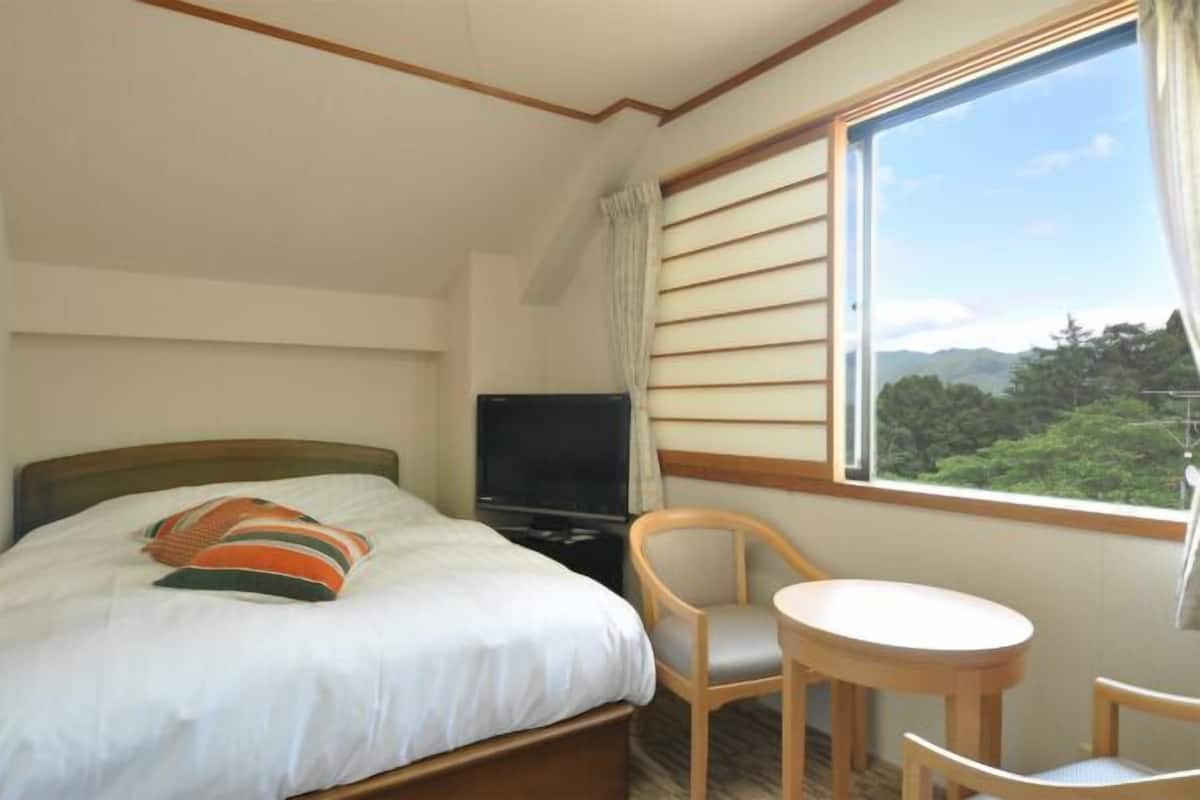 Ein Hotelzimmer mit Bett, Fernseher, kleinem Tisch und Stuhl.
