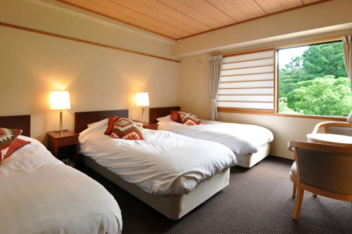 Ein Hotelzimmer mit zwei Betten, einem Sessel und einem Fenster mit Jalousien.