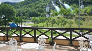 A terrace with white metal chairs and tables, overlooking a lush green landscape and a large water slide structure.