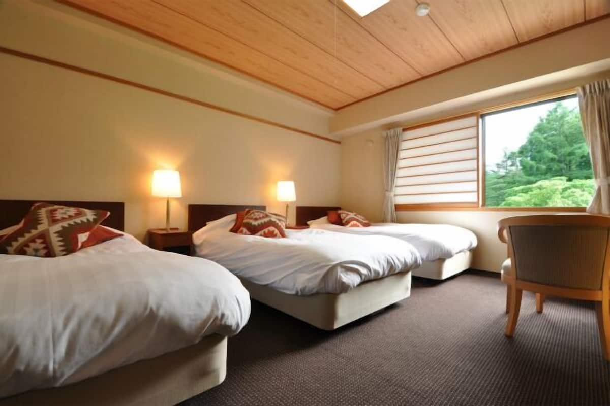 Ein Hotelzimmer mit zwei Betten, einer Holzbalkendecke und einem Fenster mit Vorhängen.