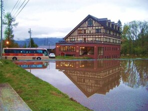 Ein traditionelles Fachwerkhäuschen mit Spiegelung im Wasser, ein Bus und ein Auto in der Nähe geparkt.