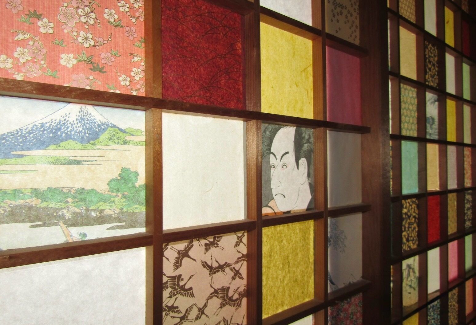 Een kamer met een traditionele Japanse shoji-schermwand, met diverse patronen en een landschapsschilderij.