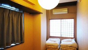 Ein kleiner, gemütlicher Raum mit Tatami-Boden, einem fensterartigen Gittermuster und zwei ordentlich bezogenen Betten.