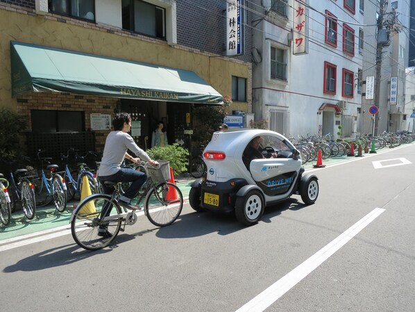 A street scene with a man riding a bicycle and a small electric car parked on the side of the road.