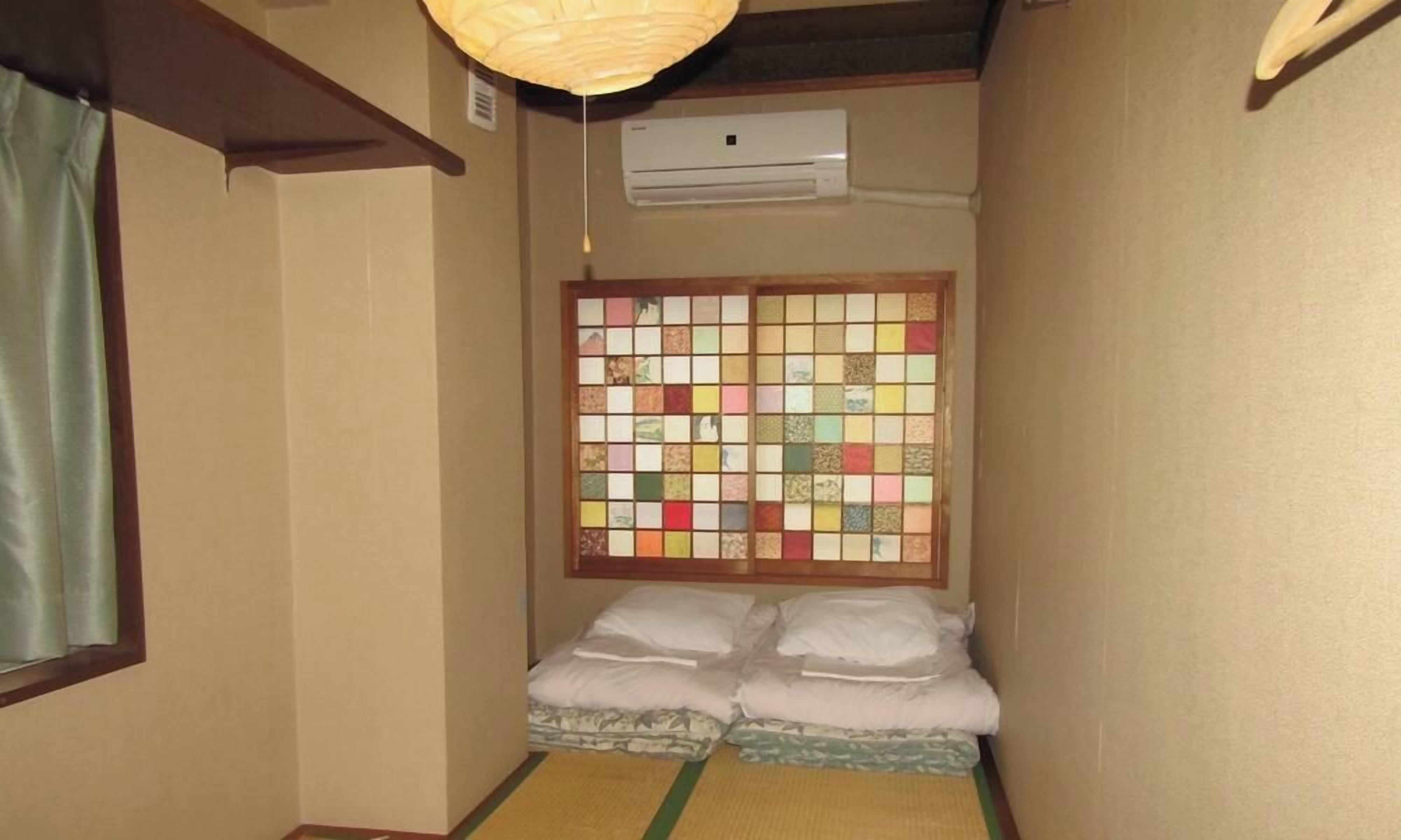 A narrow room with tatami flooring, a futon bed, a shoji screen, and an air conditioning unit.
