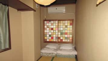 A narrow room with tatami flooring, a futon bed, a shoji screen, and an air conditioning unit.