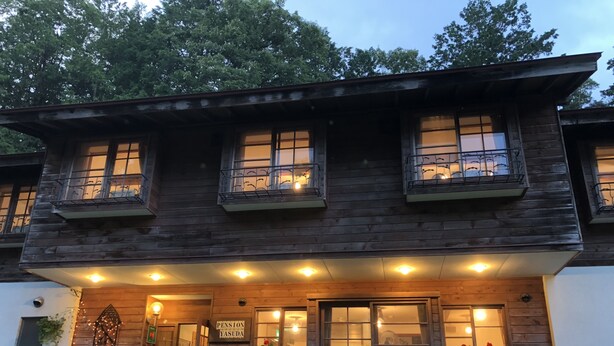 A two-story wooden building with a porch, large windows, and potted plants. - Inn of Amigos Yasuda Pension (Takayama)