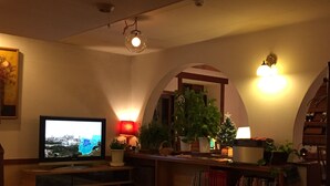 A cozy living room with a television, bookshelves, a coffee table, and a patterned rug. - Inn of Amigos Yasuda Pension (Takayama)