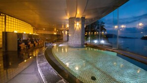 An indoor swimming pool with tiled flooring, seating areas, and a view of the sea. - Toba Grand Hotel (Toba)