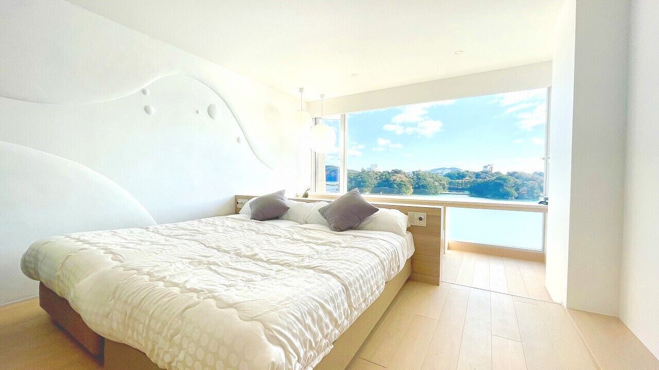 A modern bedroom with a large bed, a view of a lake, and a unique curved wall design.
