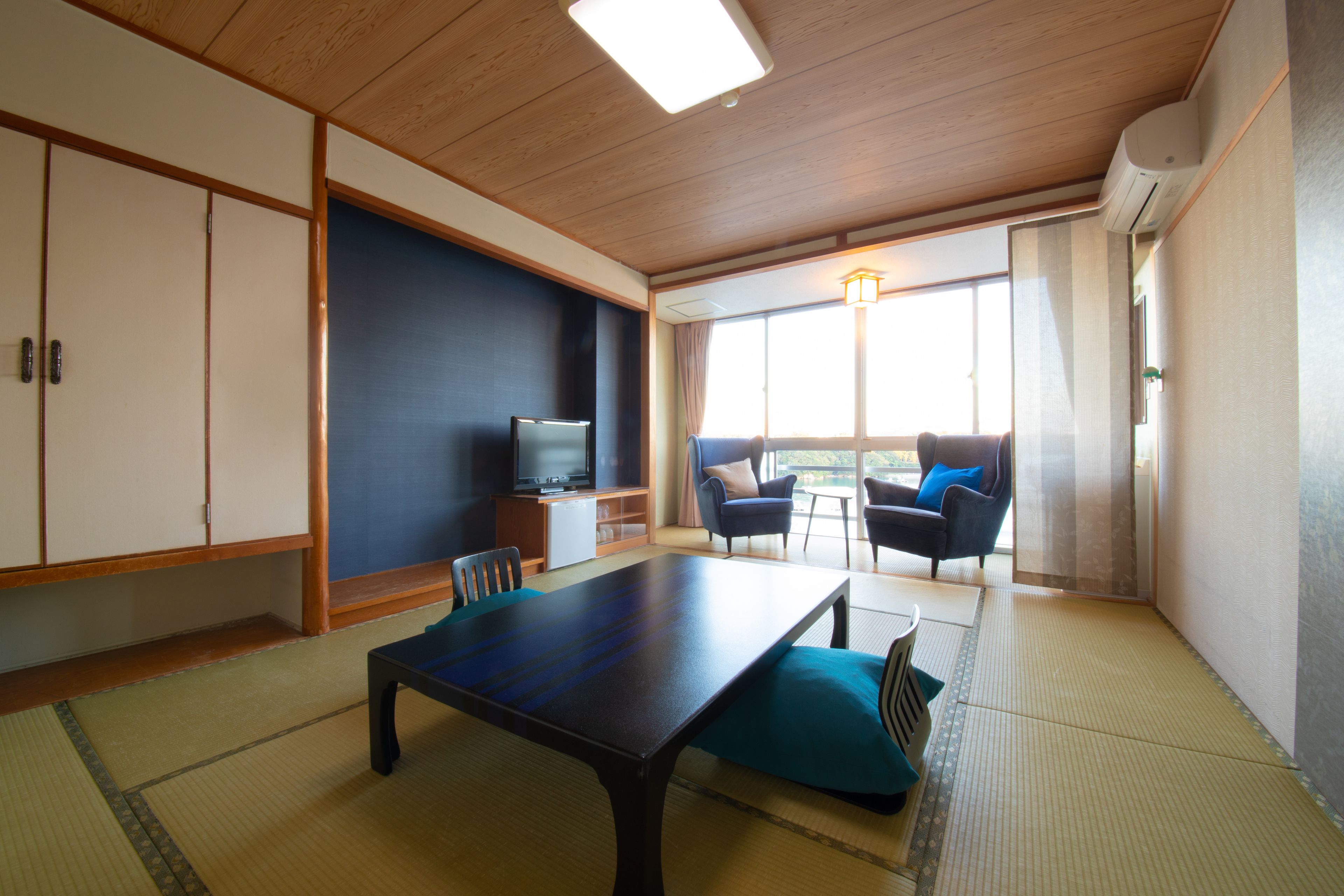 Una tradizionale stanza in stile giapponese con pavimento in tatami, un tavolino, un televisore e un divano con cuscini.