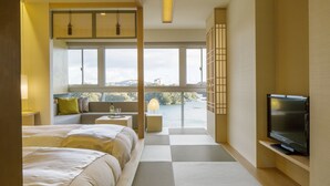 A hotel room with a large bed, a TV, a seating area with a view of the city, and a balcony. - Toba Grand Hotel (Toba)