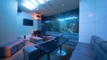 A modern lounge area with leather sofas, a central table, and a large wall-mounted screen.
