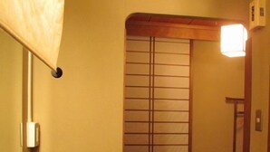 Une pièce traditionnelle japonaise avec un sol recouvert de tatamis, une basse table en bois, une bouilloire noire et une fenêtre dotée de panneaux coulissants en papier.