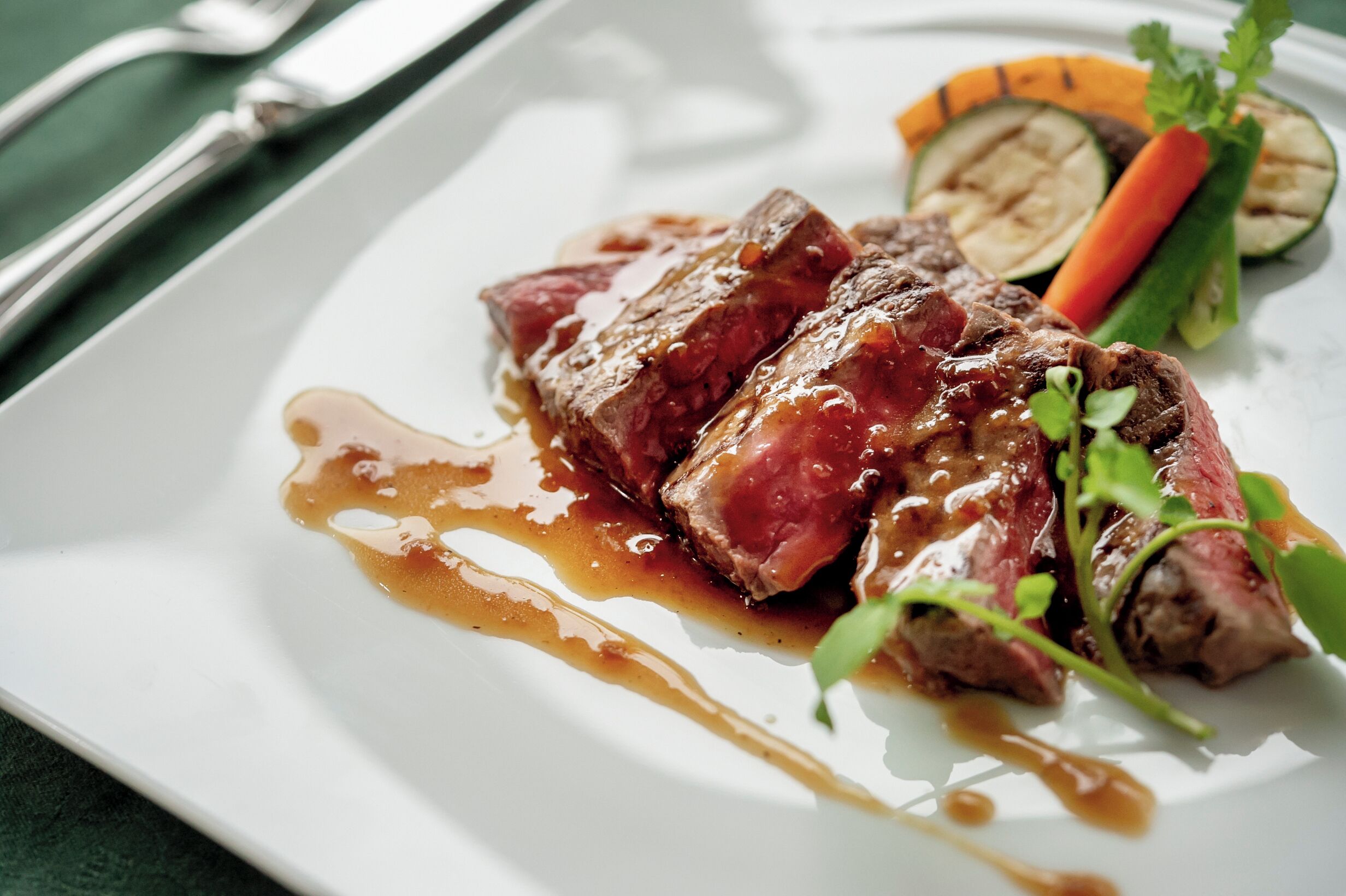 A white plate with sliced meat, vegetables, and sauce.