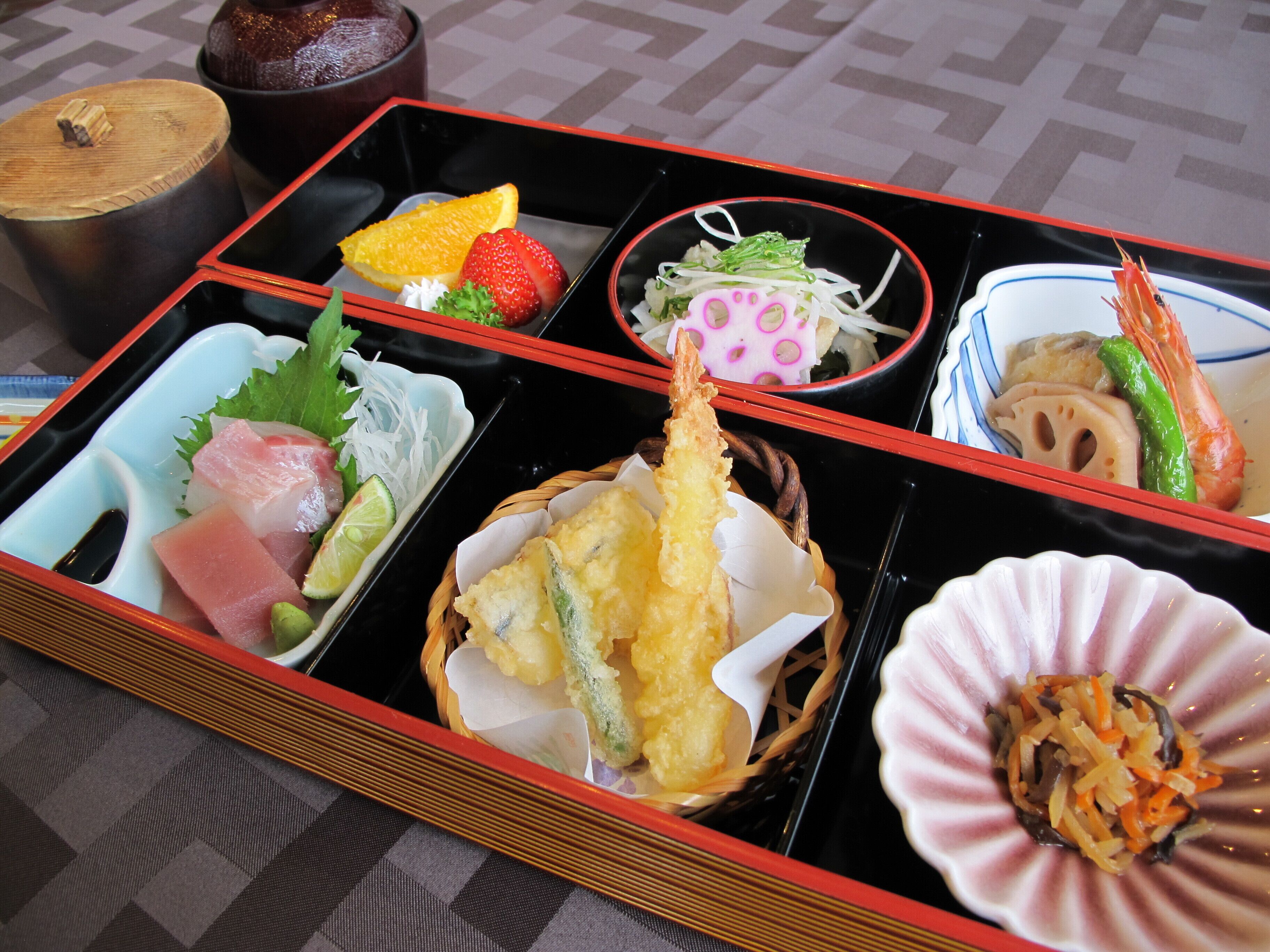 A traditional Japanese bento box with various dishes including sashimi, tempura, and a shrimp.