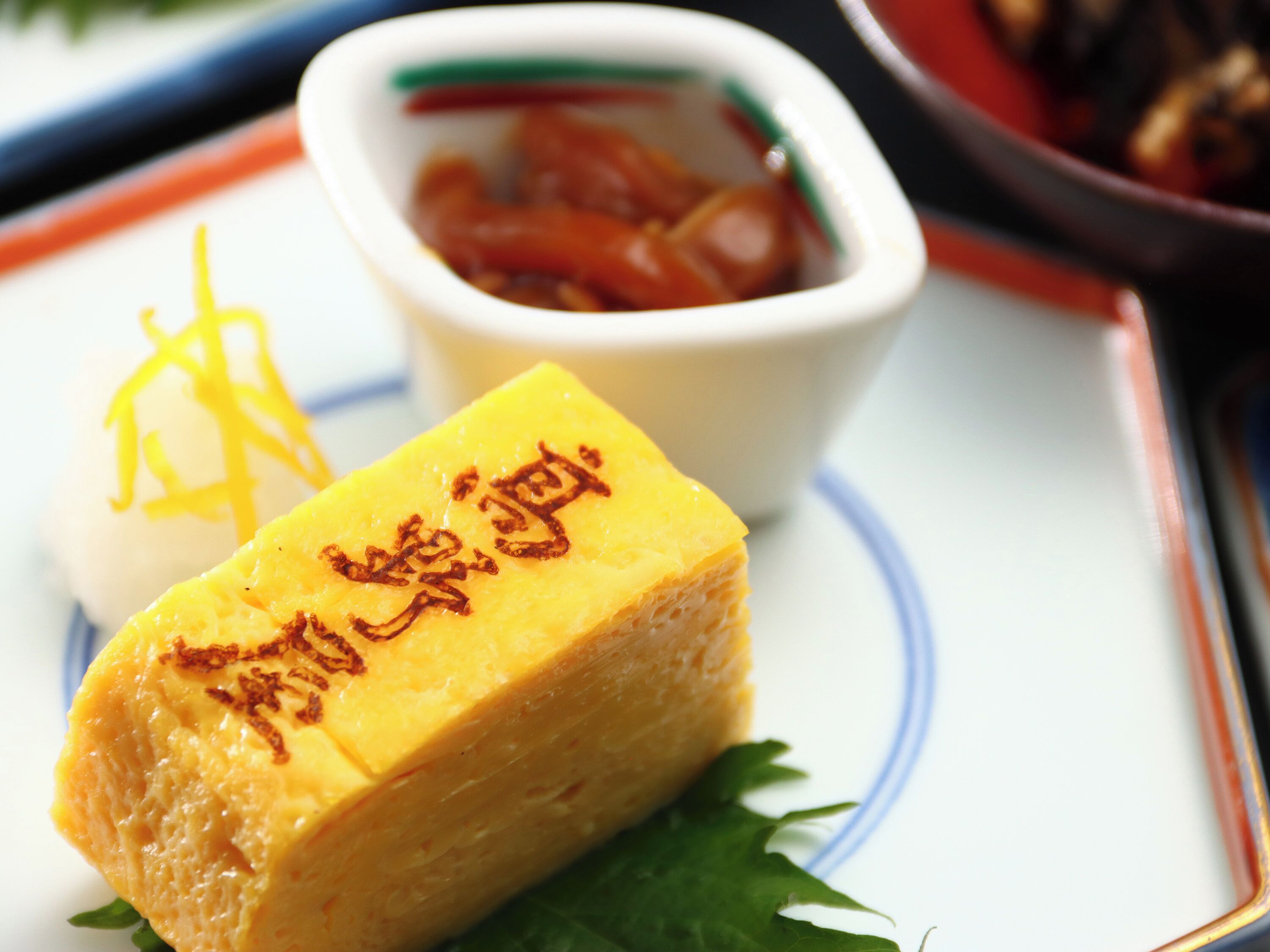 A dessert with a golden-brown top, a small bowl of sauce, and a decorative item on a plate.
