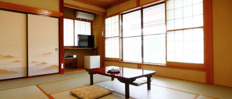 A traditional Japanese room with tatami flooring, a low table, a cushion, sliding doors, and a television.