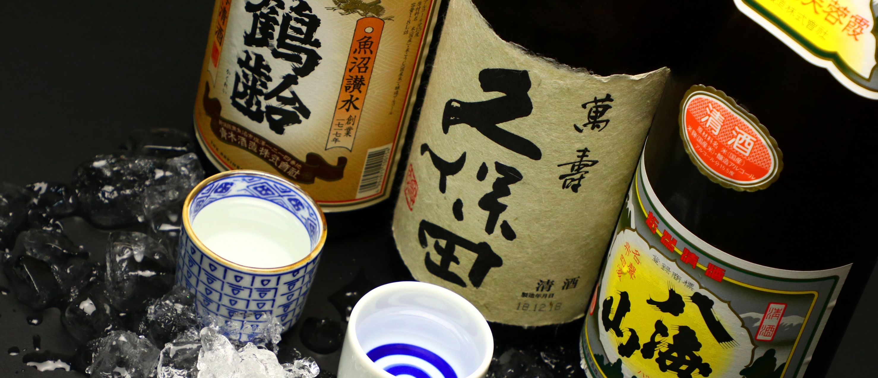 A variety of Japanese sake bottles and a ceramic cup with a blue pattern.