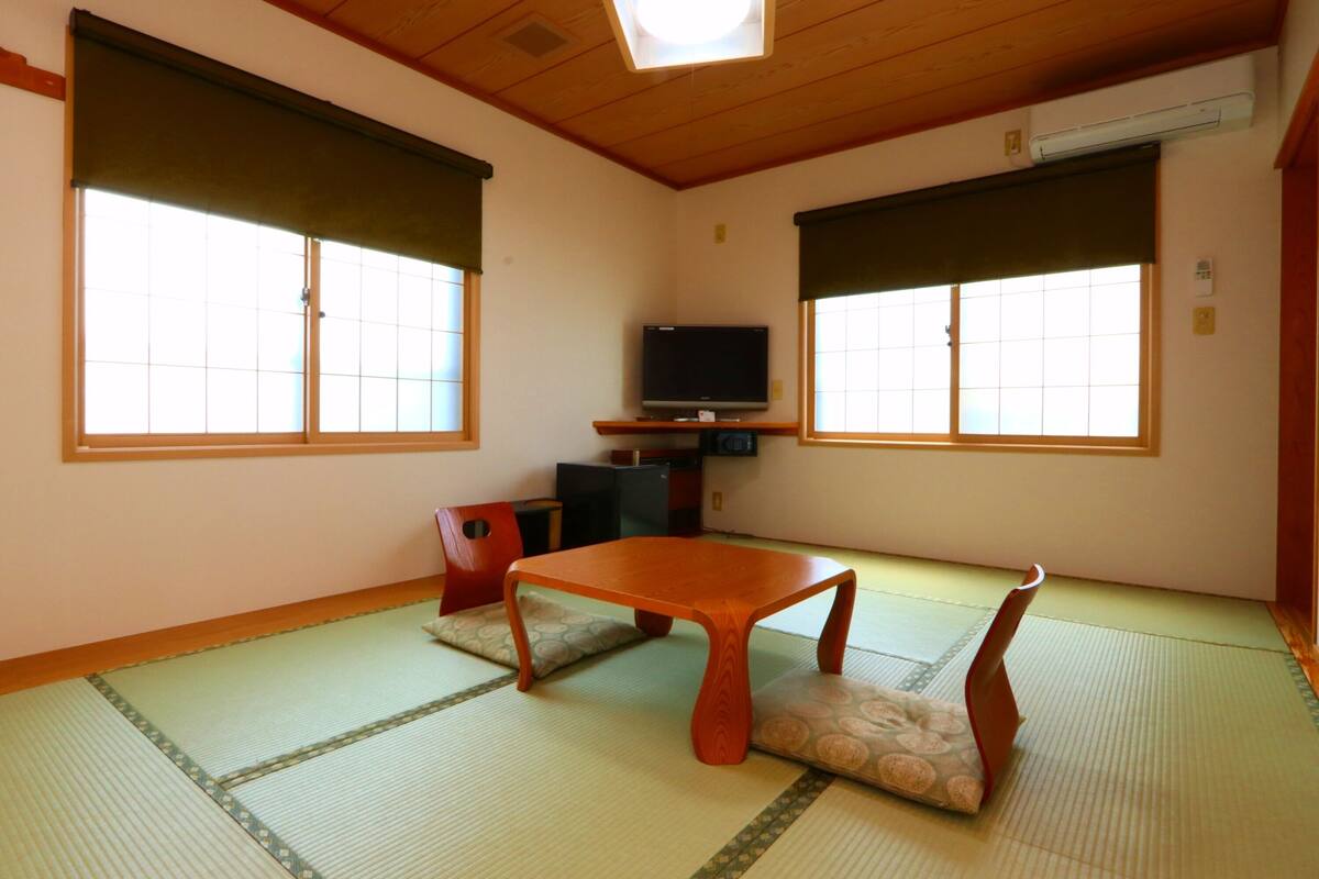 A traditional Japanese room with tatami flooring, a low wooden table, and a television on a stand.