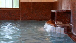 Un jacuzzi con un banco de madera y un bordeado de azulejos, rodeado por un muro de azulejos y una ventana con barrotes.