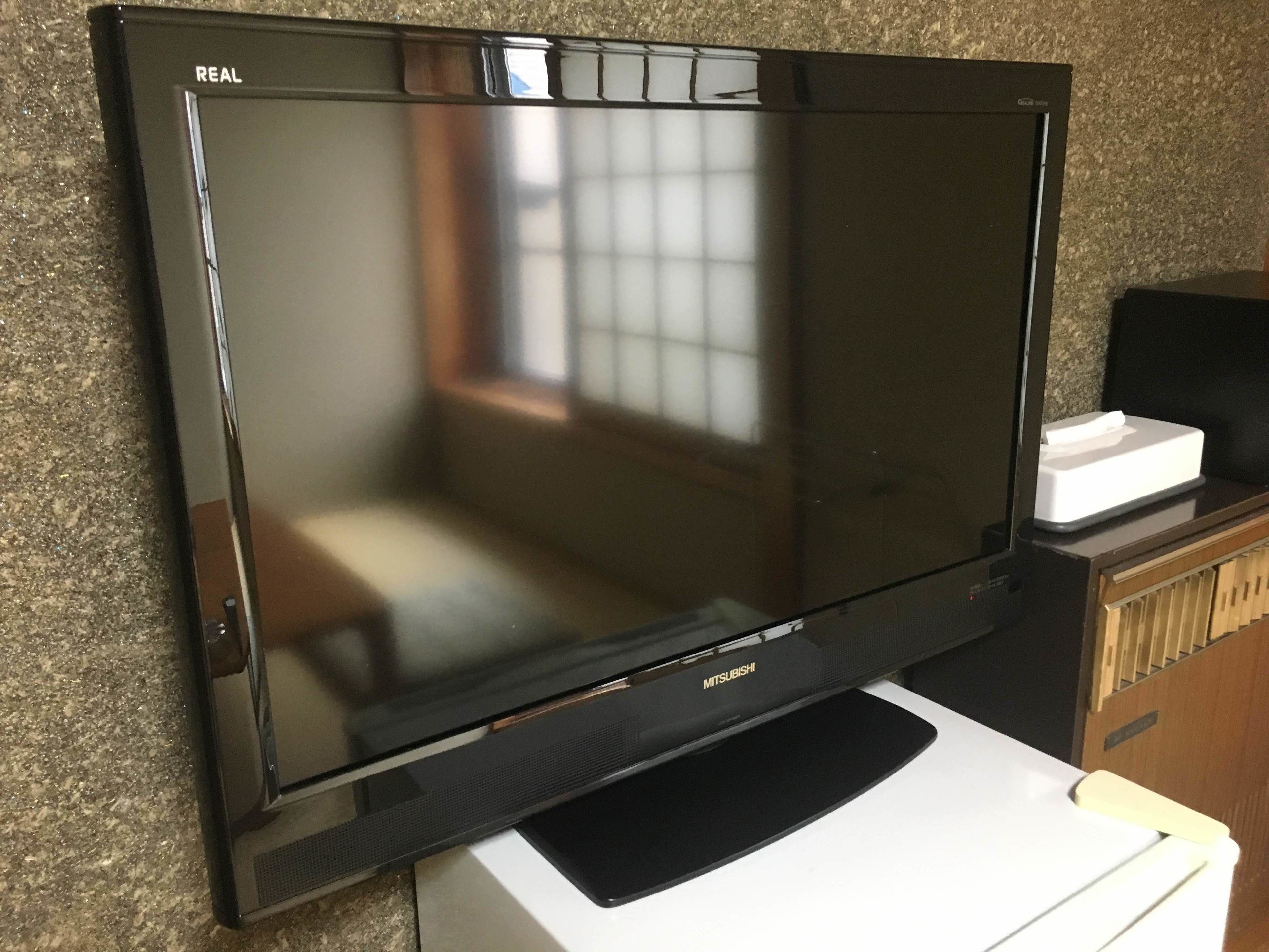 A flat-screen TV mounted on a wall, with a remote control on a stand below it.