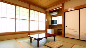 Una habitación japonesa tradicional con suelo de tatami, una mesa baja, un cojín, puertas correderas y un televisor.
