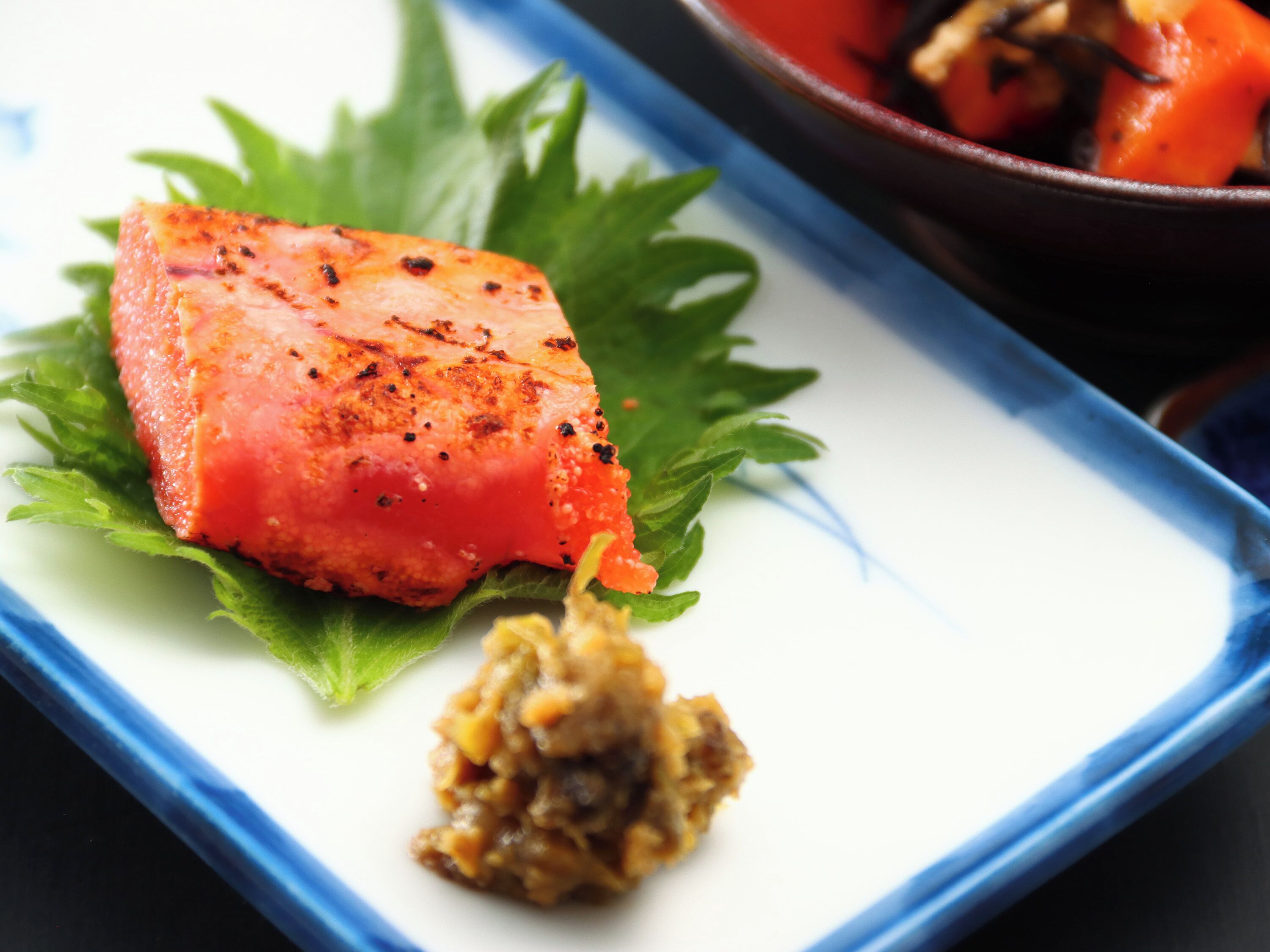 A dish with salmon on a bed of greens, accompanied by a side of sauce.