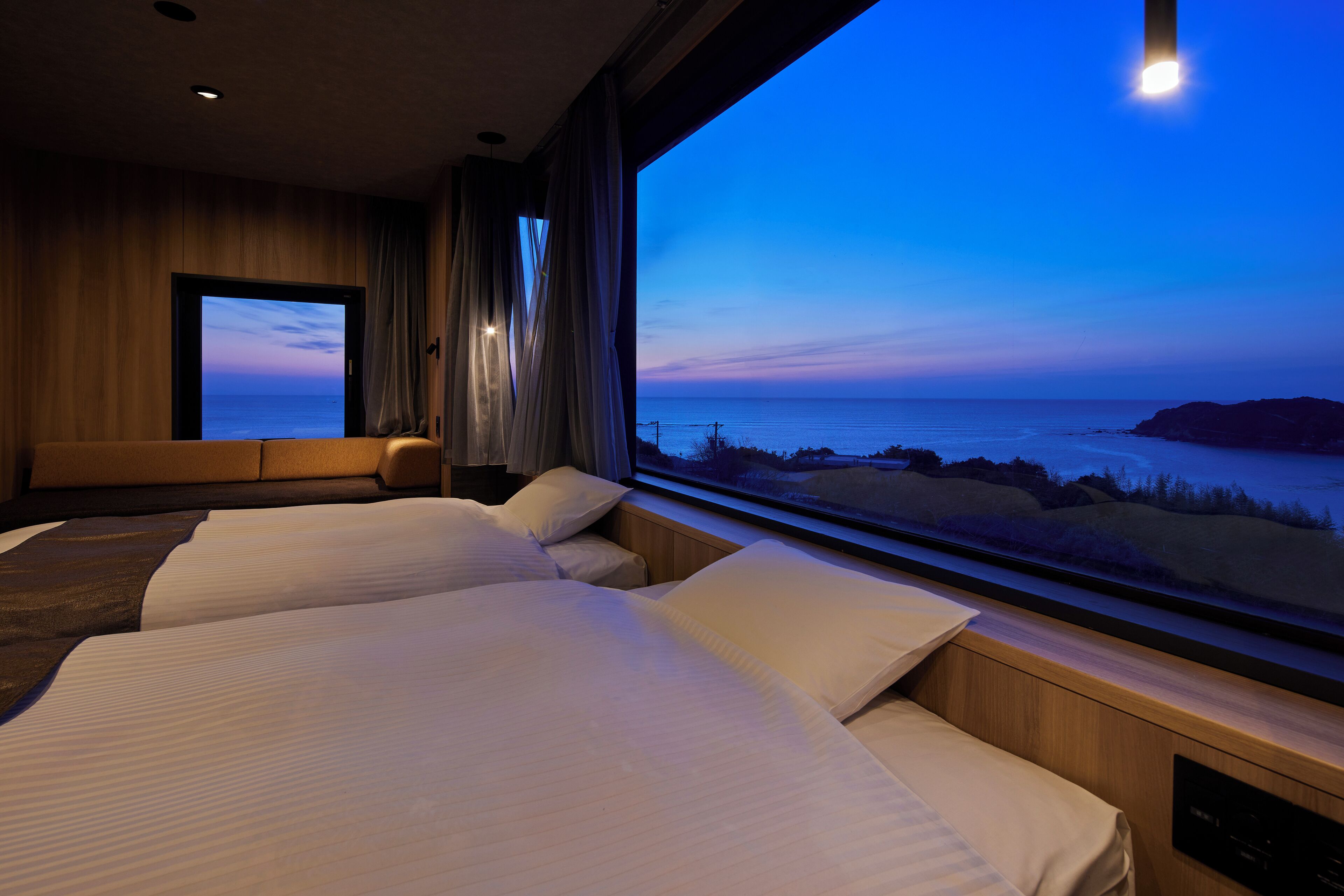 A hotel room with two beds, a large window with a view of the sea, and a wooden interior.