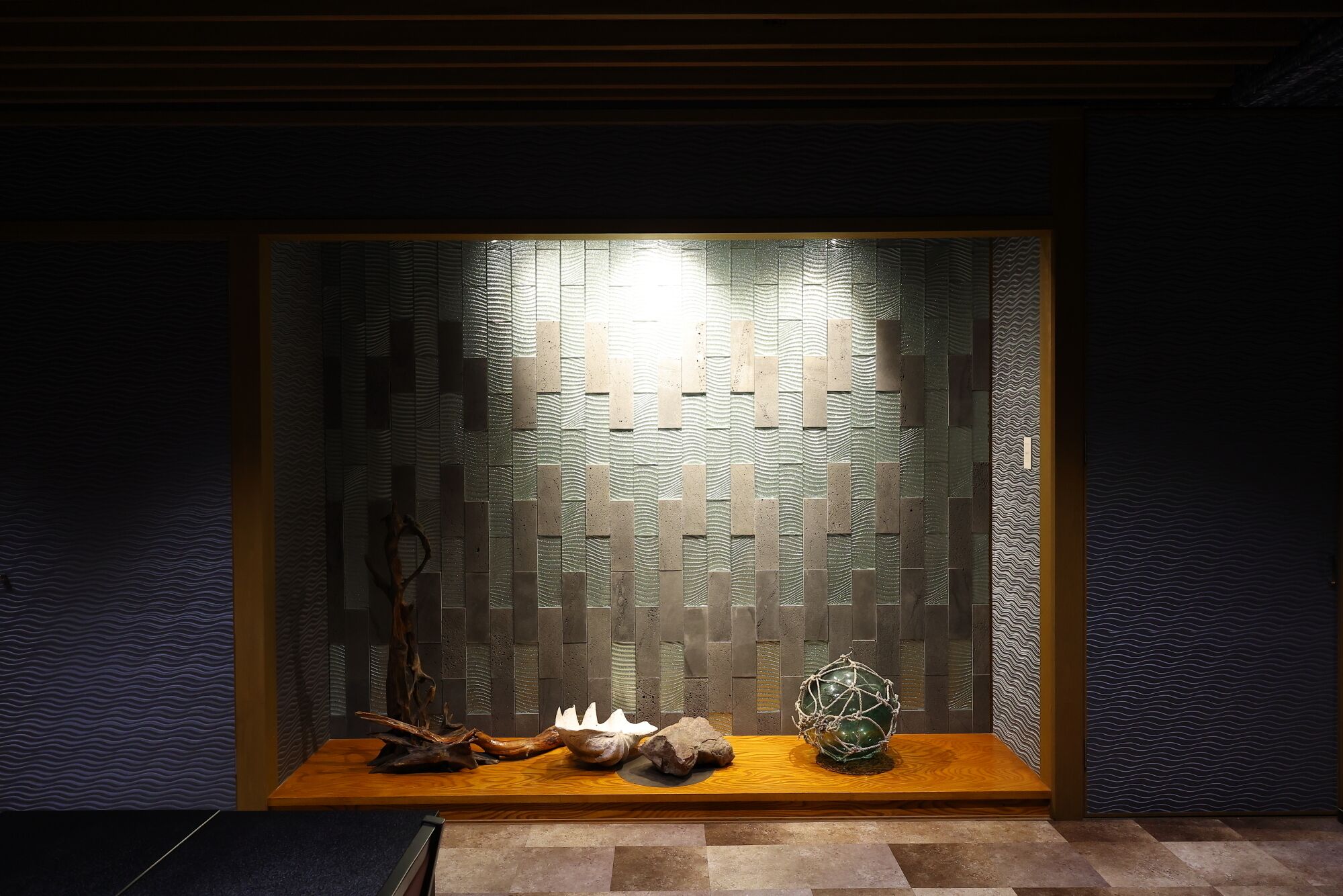 A dark room with a wooden bench, a wall with a textured pattern, and a window with a geometric design.