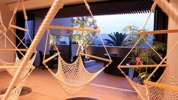 A room with three hanging hammocks, a large window with a view of palm trees and mountains, and a tiled floor.