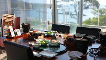 Una mesa de comedor con diversos platos y utensilios, con vistas a un cuerpo de agua y follaje a través de un ventanal grande.