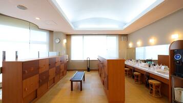 A modern hotel bathroom with wooden lockers, a bench, and a long counter with toiletries.