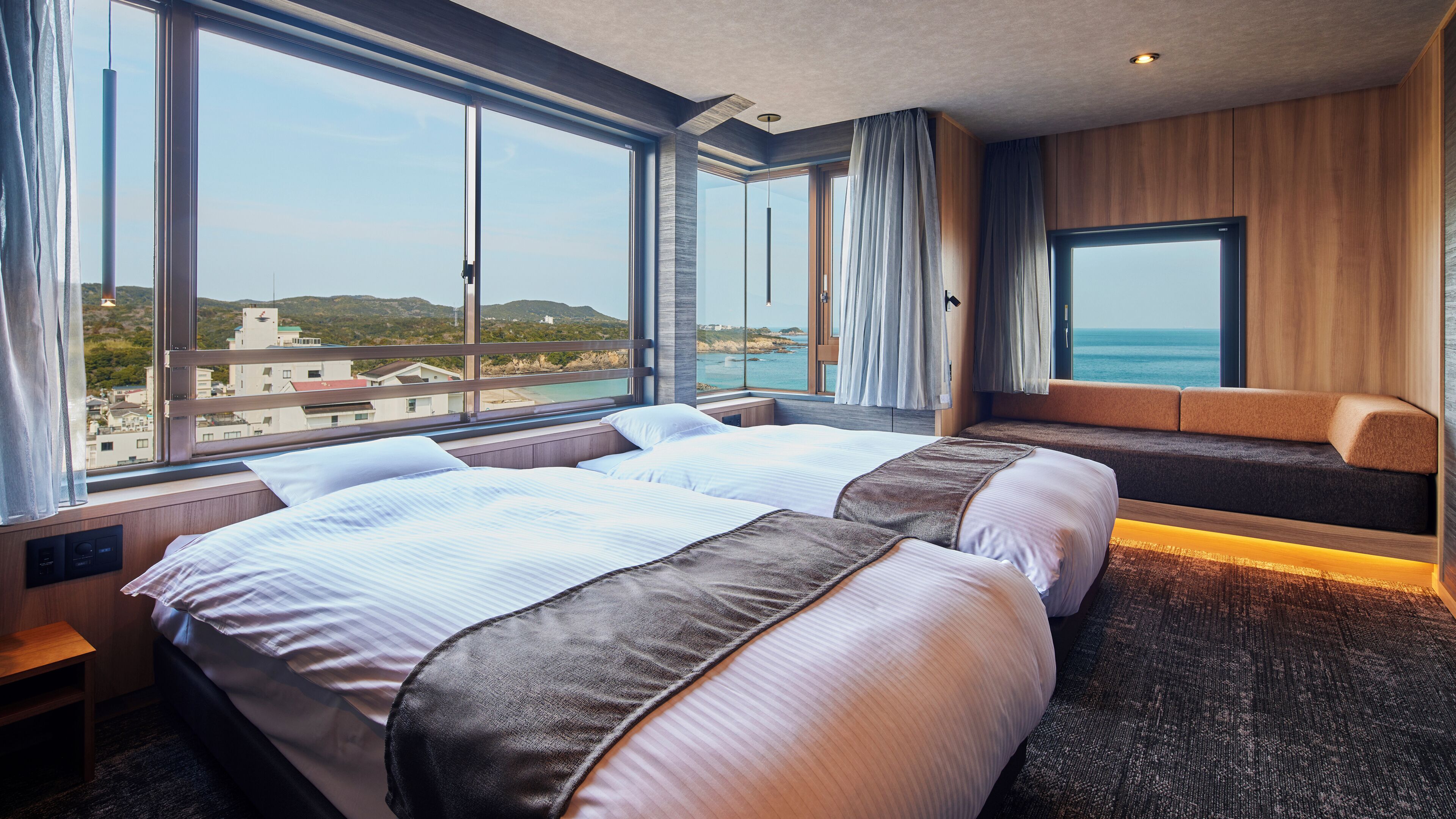 A hotel room with two beds, large windows, a view of the sea, and a wooden accent wall.