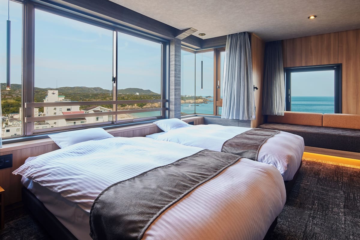A hotel room with two beds, large windows, a view of the sea, and a wooden accent wall.