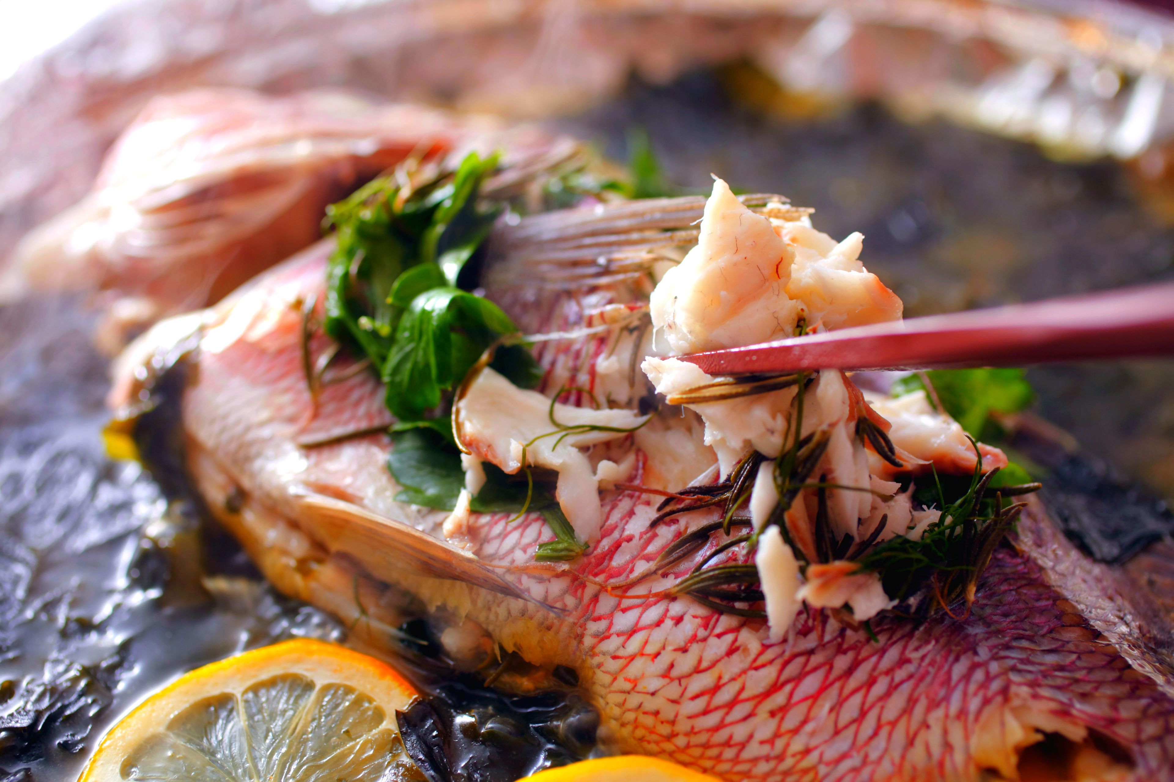 En hel fisk med örter och citronskivor på en grill eller annan tillagningsyta.