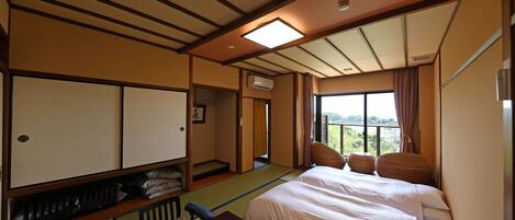 A hotel room with a bed, a table, and a view of greenery outside.