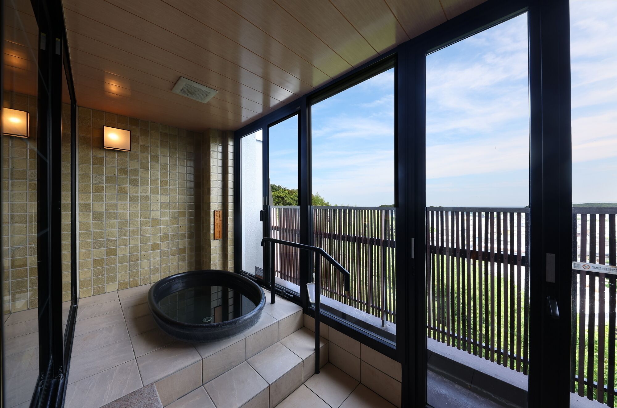 A modern bathroom with a glass-enclosed shower, a circular bathtub, and a view of the sea through large windows.