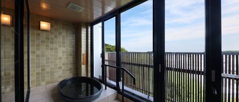 A modern bathroom with a glass-enclosed shower, a circular bathtub, and a view of the sea through large windows.