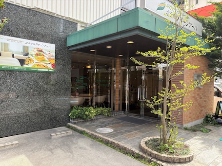 A hotel entrance with a glass door, a green awning, and a signboard.. Hotel Green Arbor