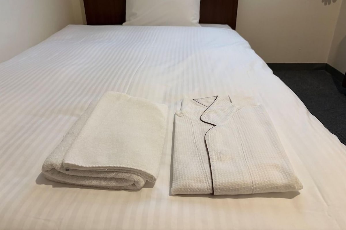 A neatly made bed with a white bedspread and two folded towels.