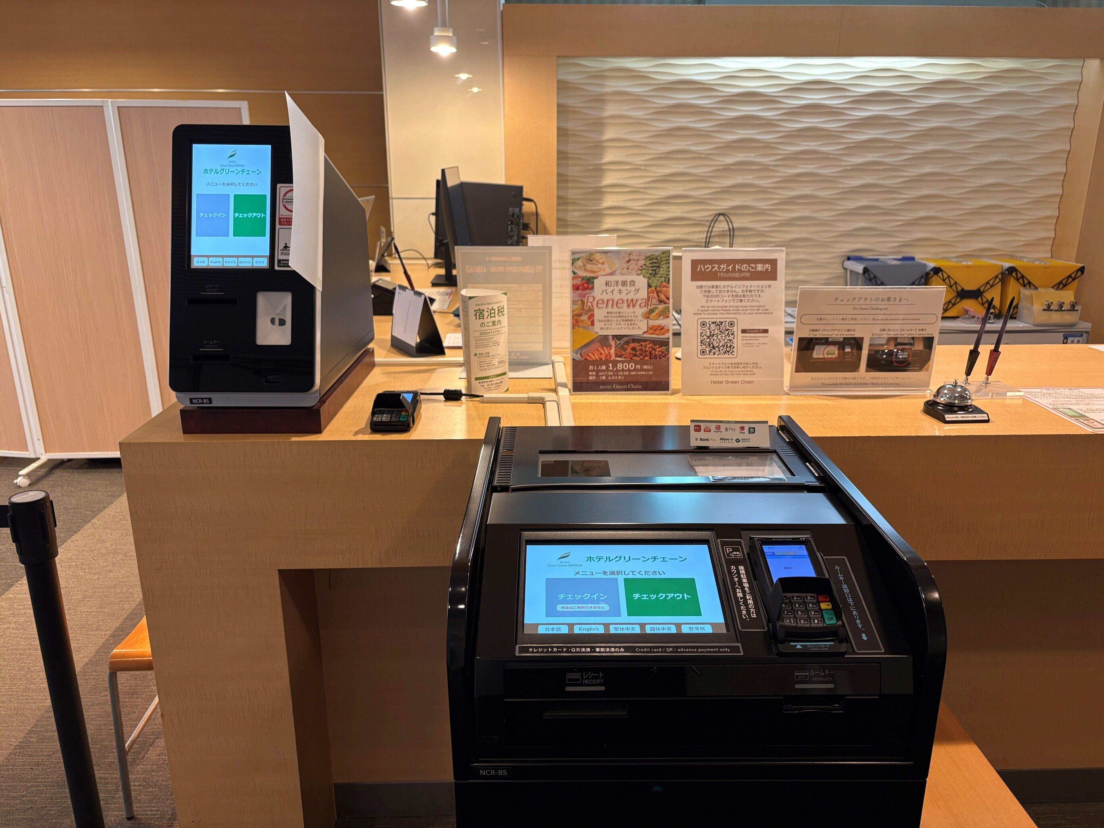 A hotel reception area with a NCR-85 terminal, a cashless payment station, and informational signs.