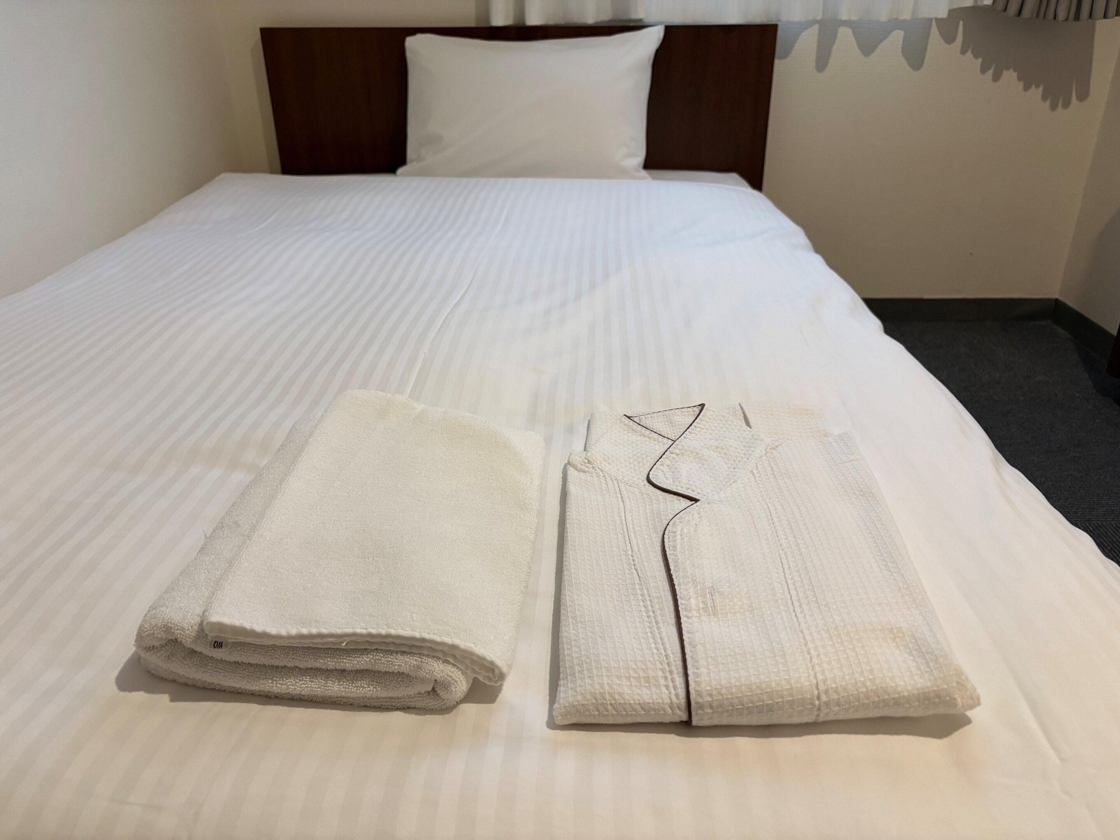 Cama bem arrumada com lençóis brancos e uma toalha dobrada ao lado.
