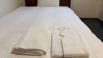 A neatly made bed with white linens and a folded towel on the side.