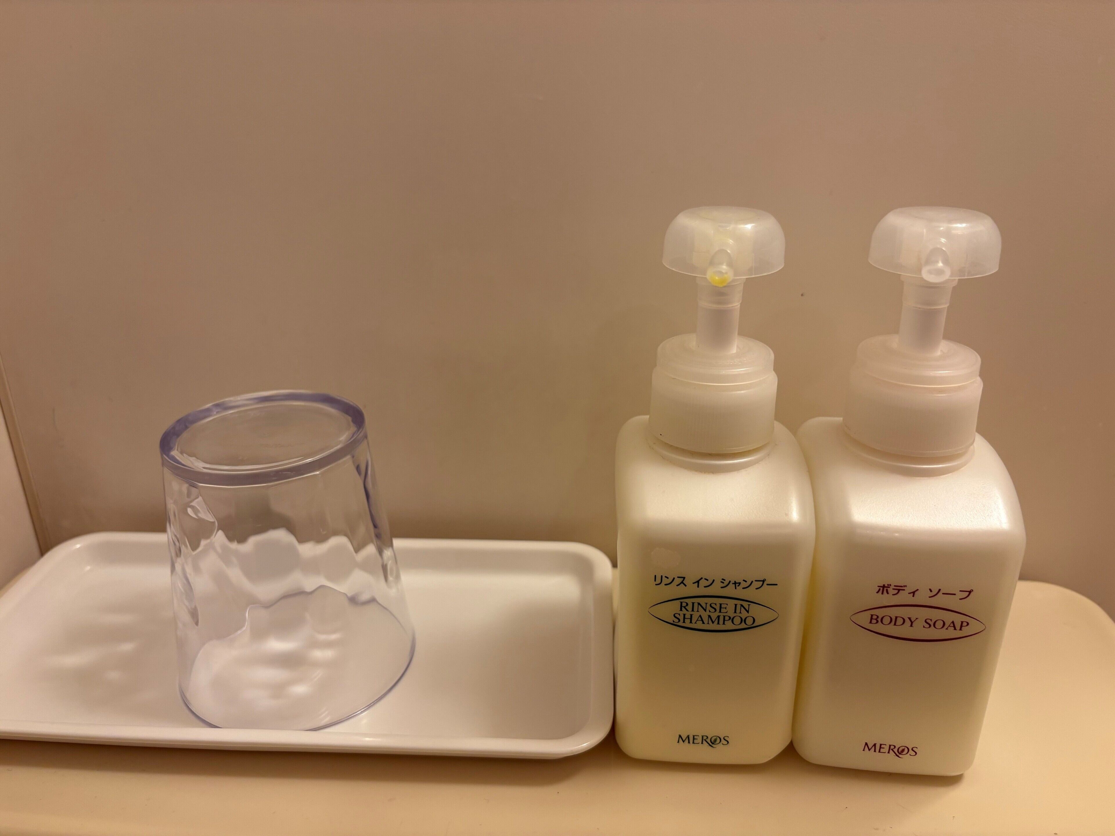 A bathroom with a white sink, a glass, and two bottles of body soap.
